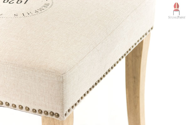 Die Kombination der bronzefarbenen Nieten, den geschwungenen Holzbeinen und dem braunen Stoffbezug überzeugen